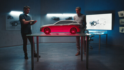 Senior automotive engineers examine the prototype car model placed on a glass table in different...