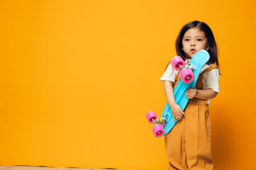 a cute, adorable little preschool girl stands with a blue skateboard in her hand, smiling adorably at the camera. Horizontal photo with empty space to insert an advertising layout