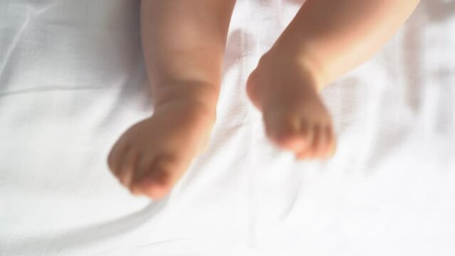 Newborn baby feet on the bed. The legs of a newborn baby move on a white sheet. The concept of motherhood, family, birth. High quality 4k footage
