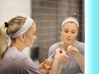 woman looking in the mirror in the bathroom and taking care of her skin.