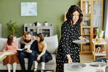 Portrait of Jewish family at home with focus on young woman setting table with silverware, copy...