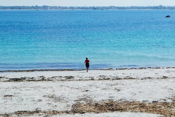 Fototapeta na wymiar Child in red top running towards the azure blue sea