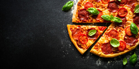 Pizza on black background. Traditional italian pizza with salami cheese, tomatoes and basil. Top view with copy space.