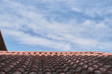Tiled roof against a blue sky with clouds, an idea for a background with space for text. Eco-friendly traditional roofs for the home