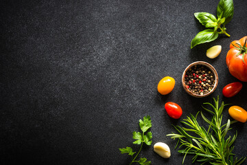 Food background on black stone table with fresh vegetables, herbs and spices. Ingredients for cooking with copy space.