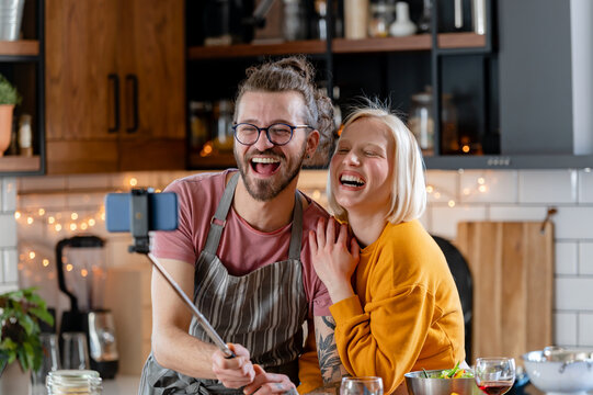 Young cheerful love couple at home during holidays talking with friends making video call using smartphone. Having fun. Happiness concept.