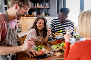 Young diverse people having a holiday party at home, preparing food, drinking, talking, and enjoying