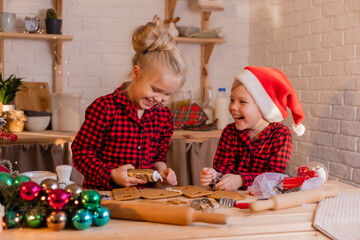 boy and girl in red christmas pajamas prepare a gingerbread house and decorate it with icing at home