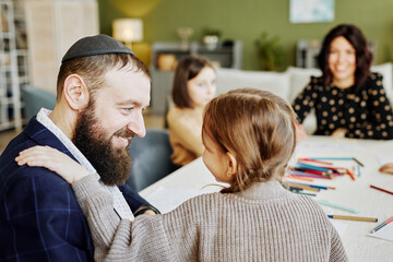 Side view portrait of smiling jewish man playing with children at home with family in background