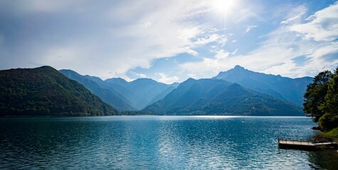 Obraz premium Beautiful lake, a small dock and mountains with a sunny sky in the background.