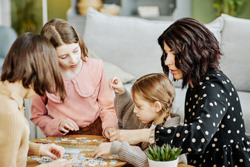 Side view portrait of young mother with three children playing with puzzle together in home setting