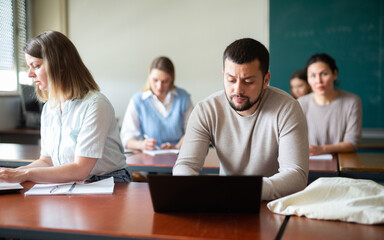 Obraz premium Handsome adult male student typing on laptop during lecture at university