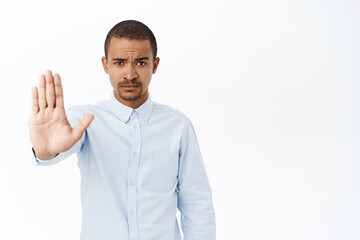 Concerned young office worker, man shows stop sign and looking worried, decline smth, prohibit,...