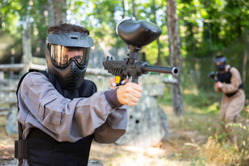Fototapeta premium Woman targeting with paintball gun to eliminate enemies on battlefield. Markswoman shooting with paintball marker.