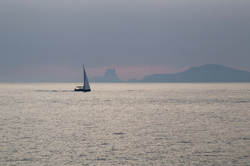 Sailboat sailing in the Mediterranean during sunset with an island behind