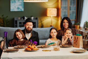 Portrait of modern jewish family looking at camera while sitting at dinner table in cozy home...