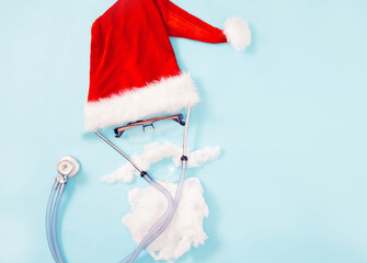The concept of a doctor in a santa claus hat with a beard in glasses with a stethoscope on a blue background. copy space. Flat lay. Health and medicine banner for Christmas, happy new year