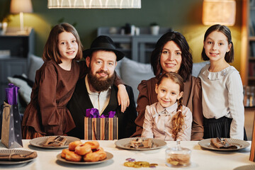 Portrait of orthodox jewish family looking at camera while sitting at dinner table in cozy home...