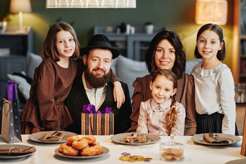 Portrait of orthodox jewish family looking at camera while sitting at dinner table in cozy home setting