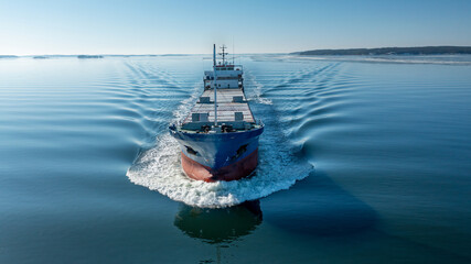 Aerial forward view of general cargo vessel making way ahead in Finnish archipelago during spring...