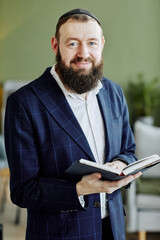 Vertical portrait of bearded jewish man wearing kippah and looking at camera holding book