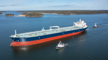 Tug boats escort large crude oil carrier through narrow Finnish archipelago. Ship's hull recently...