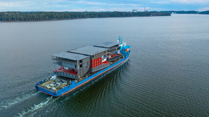 Heavy load carrier transporting large ship building blocks on deck in Finnish archipelago. Aerial side view.