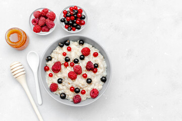 Oatmeal porridge with summer raspberry, currant berries,honey. Porridge oats in bowl with fruits. Healthy food breakfast,lifestyle,dieting, proper nutrition.Top view flat lay on gray table background