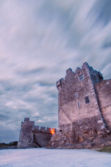 Ancient old Fortress Ross Castle ruin with a lake, green grass and orange clouds. Killarney...