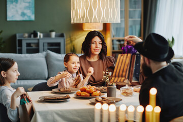 Portrait of modern jewish family enjoying dinner together at home and playing dreidel, copy space