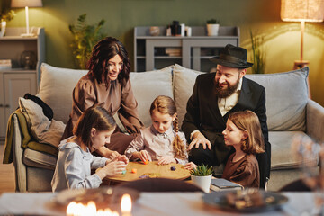 Portrait of modern jewish family playing traditional dreidel game in cozy home setting