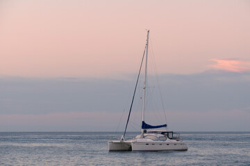 Single-deck sailing yacht on the sea in calm. Lonely empty boat at sunset during the golden hour. A boat against a pink-blue sky.