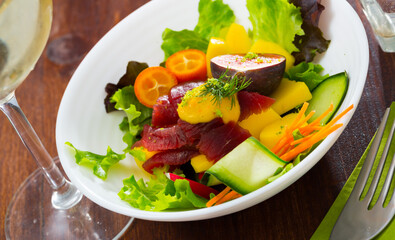 Colorful salad with raw tuna, greens, cucumbers mango figs carro, radish and kumquat