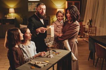 Portrait of modern jewish family lighting silver menorah candle during Hanukkah celebration in cozy...