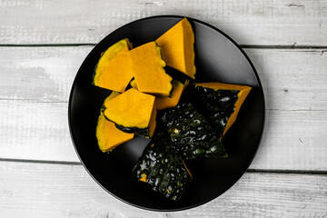 Pumpkin or Jerimum cut into pieces on a black plate on a wooden background. From the family Cucurbitaceae and genera Abobra and Cucurbita rich in vitamins and very used to make sweets and purees.