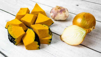 Pumpkin or Jerimum cut into pieces on a wooden background with garlic and onion. From the family...