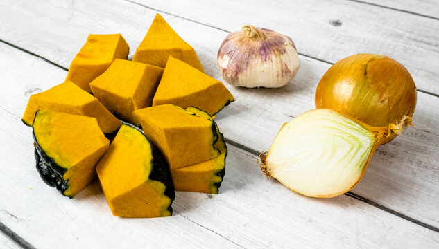 Pumpkin or Jerimum cut into pieces on a wooden background with garlic and onion. From the family Cucurbitaceae and genera Abobra and Cucurbita rich in vitamins and very used to make sweets and purees.