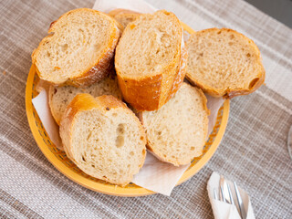 Bread sliced and served on table in wicker plate with serving pieces.