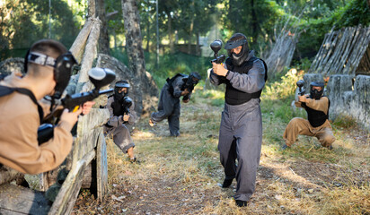 Team eliminating opponents on paintball field. People in protective outwear and helmets aiming with paintball markers.