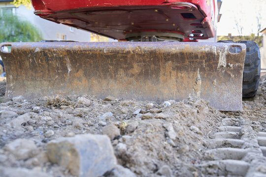 Excavator On A Construction Site Photographed From Behind At Ground Level. Dozer Blade Is Visible. Space For Text.