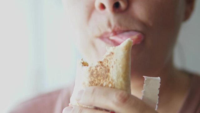 The girl eats junk food, bites, chews, and licks her lips. A woman holds pita bread with filling in her hands, close-up video. A person eats shawarma.