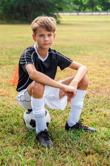 Fototapeta premium Child Youth Boy Siting on Soccer Ball on Soccer Field