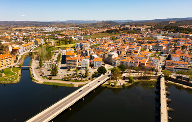 Fototapeta na wymiar Scenic drone view of Mirandela, small Portuguese city on banks of Tua overlooking terracotta roofs of residential buildings and two bridges across river on sunny spring day