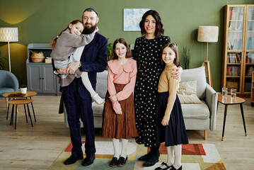 Full length portrait of happy jewish family standing in modern home and looking at camera with women and girls wearing dresses - obrazy, fototapety, plakaty