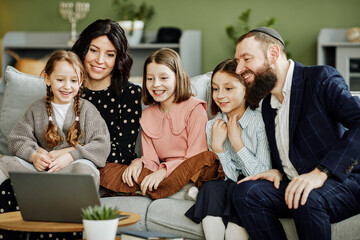 Portrait of modern jewish family using laptop and calling by video chat in cozy home setting