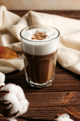 coffee latte with foam in a glass on a wooden table. next to a branch of cotton, dry leaves and a white plaid