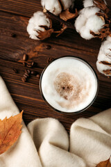 Obraz na płótnie Canvas coffee latte with foam in a glass on a wooden table. next to a branch of cotton, dry leaves and a white plaid