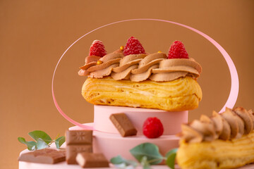  custard cakes.Eclairs cakes with chocolate cream and raspberries on a pink podium on a brown background.Choux pastry.
