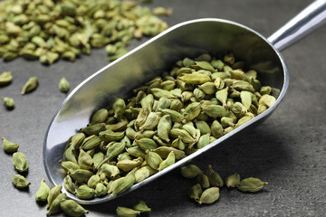 Scoop with dry cardamom pods on dark grey table, closeup