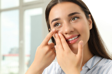 Woman putting contact lens in her eye at home